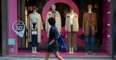 A woman walks past a shop window displaying autumn clothes in Barcelona, Spain, Oct. 27, 2022. (AFP Photo)