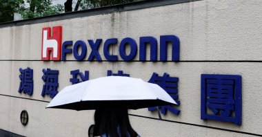 A woman carrying an umbrella walks past the logo of Foxconn outside a company's building in Taipei, Taiwan, Oct. 31, 2022. (Reuters Photo)