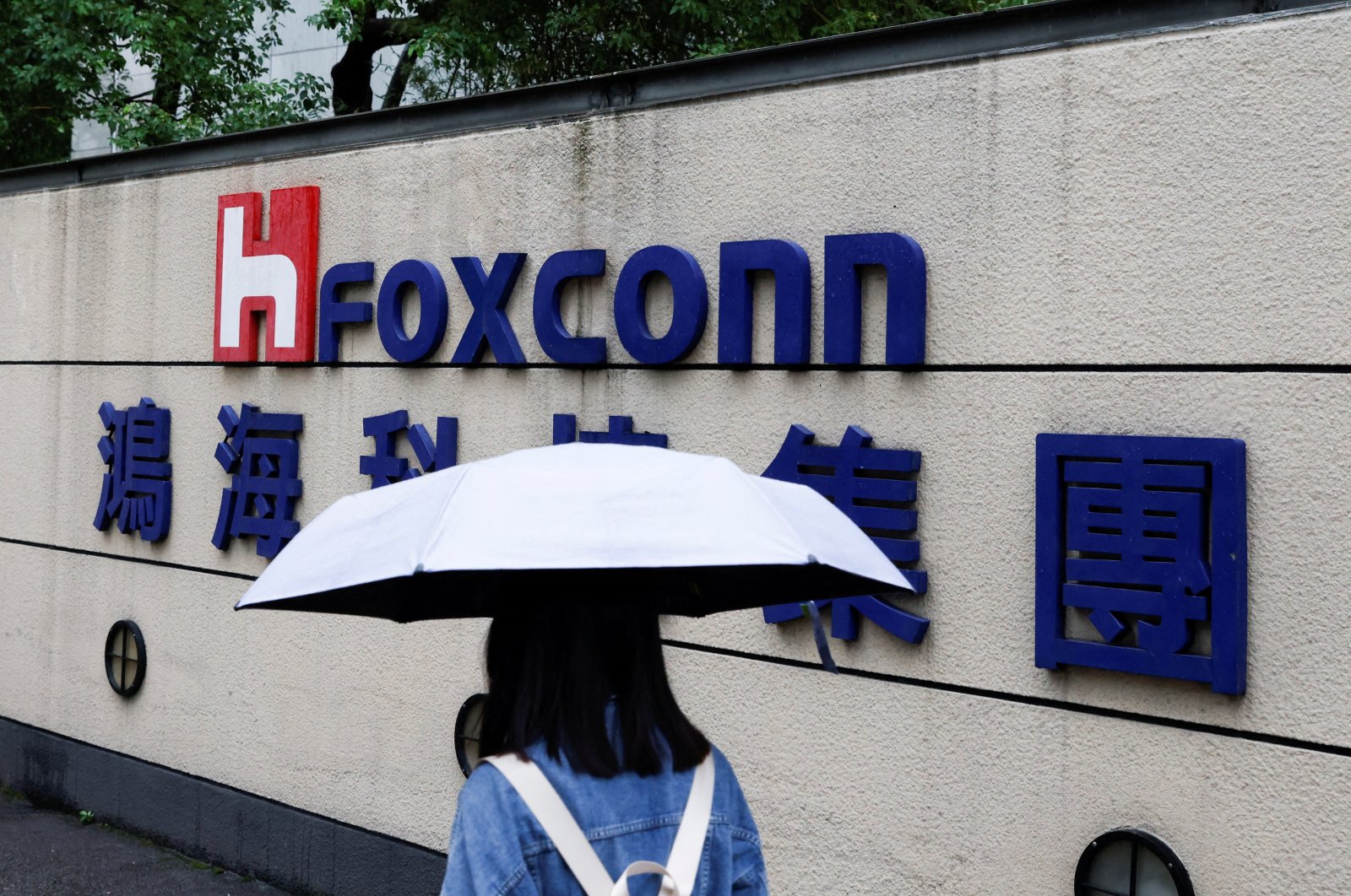 A woman carrying an umbrella walks past the logo of Foxconn outside a company&#039;s building in Taipei, Taiwan, Oct. 31, 2022. (Reuters Photo)