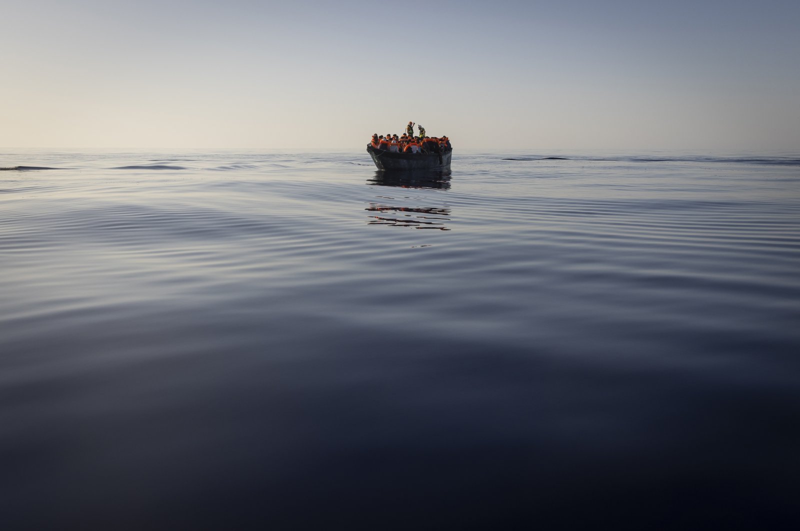 Migrants with life jackets provided by volunteers of the Ocean Viking, a migrant search and rescue ship run by NGOs SOS Mediterranee and the International Federation of Red Cross (IFCR), still sail in a wooden boat as they are being rescued in the Mediterranean Sea, Aug. 27, 2022. (AP Photo)
