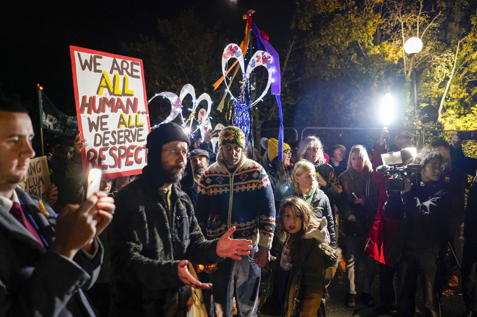People hold lights and placards, in a show of support for migrants being detained inside the Manston immigration short-term holding facility, Kent, England, Nov. 2, 2022. (AP Photo)
