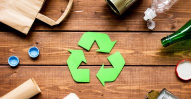 This illustration shows the waste recycling symbol encircled by different types of disposable packages on a wooden table. (Shutterstock Photo) 
