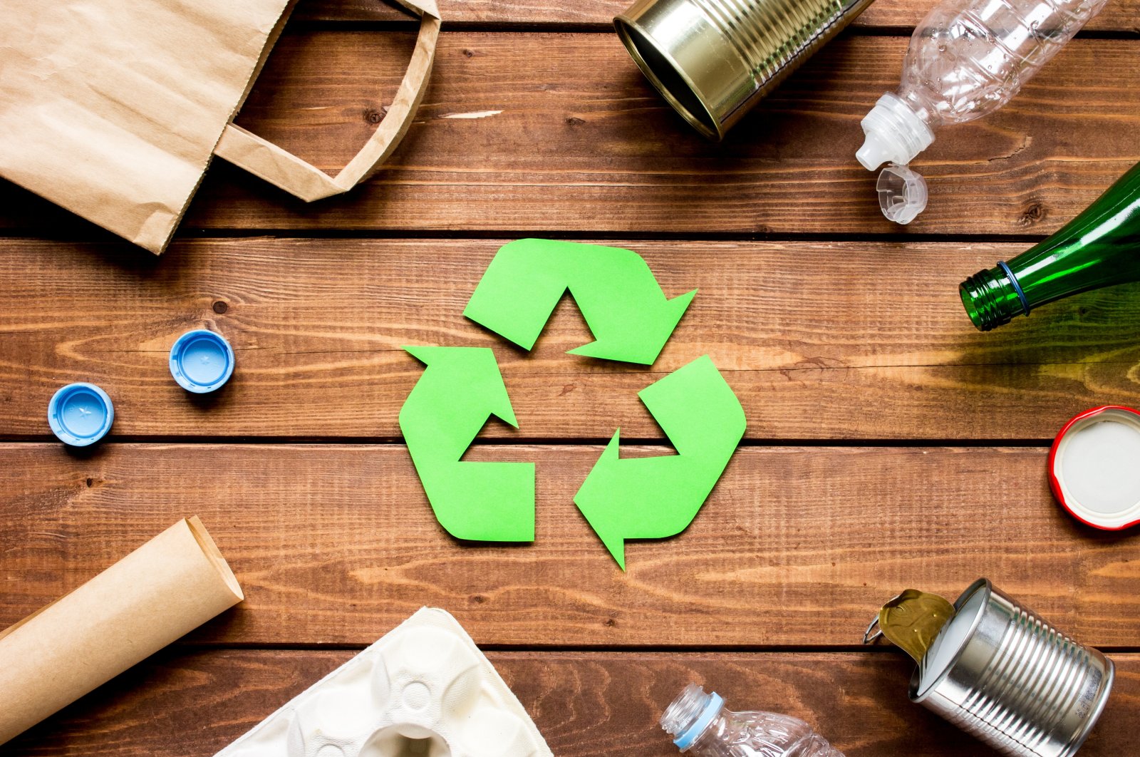 This illustration shows the waste recycling symbol encircled by different types of disposable packages on a wooden table. (Shutterstock Photo) 
