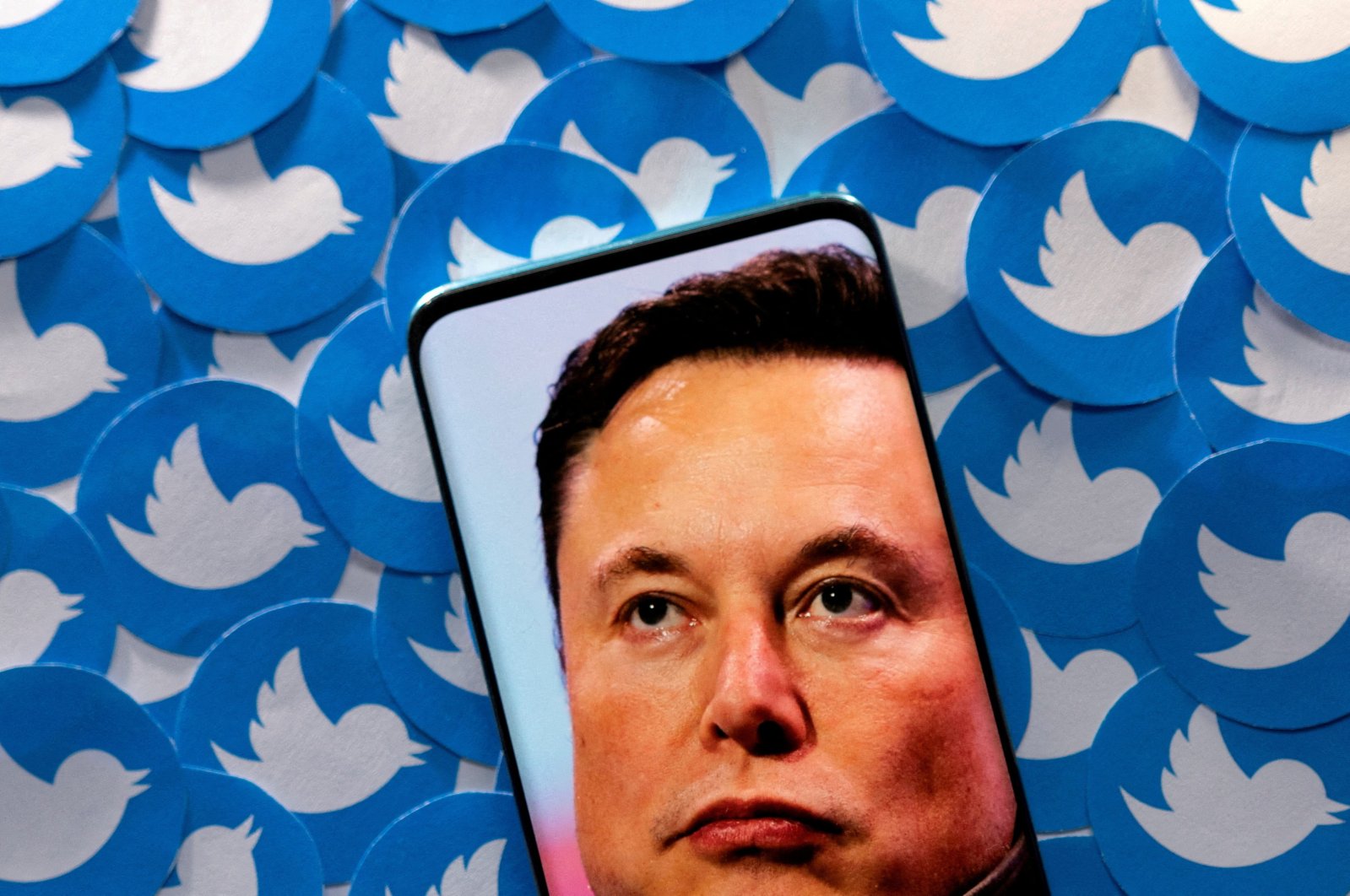 An image of Elon Musk is seen on a smartphone placed on printed Twitter logos in this photo illustration created on April 28, 2022. (Reuters Photo)