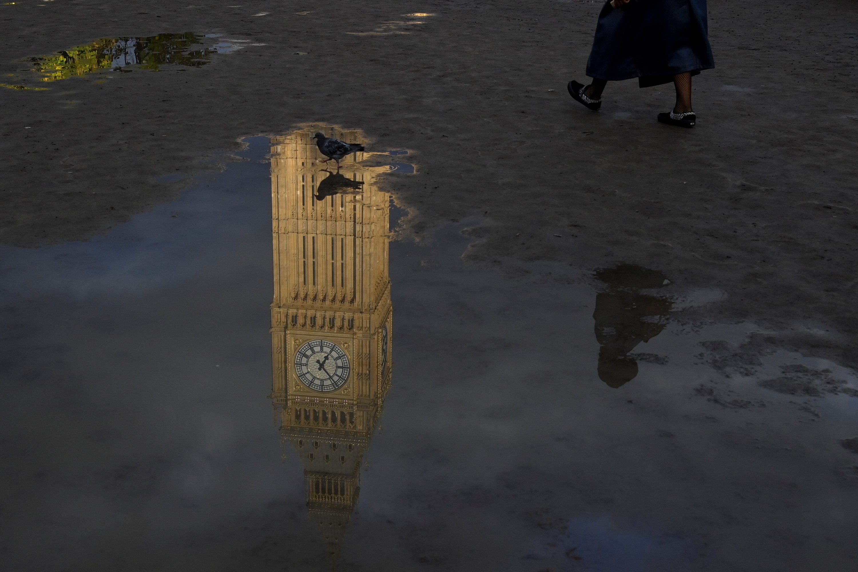 Elizabeth Tower, lebih dikenal sebagai Big Ben, tercermin dalam genangan air saat seseorang berjalan di Parliament Square, di London, Inggris, 20 Oktober 2022. (Foto Reuters)