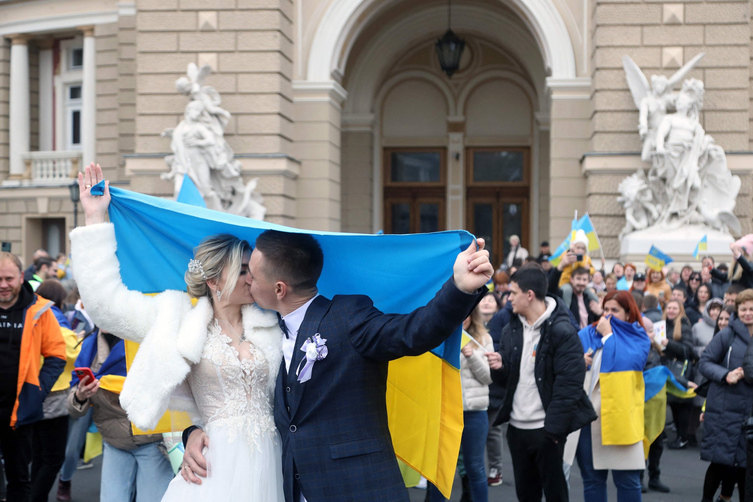 Pengantin baru, memegang bendera Ukraina, berciuman saat merayakan pembebasan kota asal mereka, Odessa, Ukraina, 12 November 2022. (AFP Photo)
