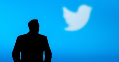 The silhouette of Elon Musk is seen in front of blue banner with Twitter logo in background. (Shutterstock Photo)