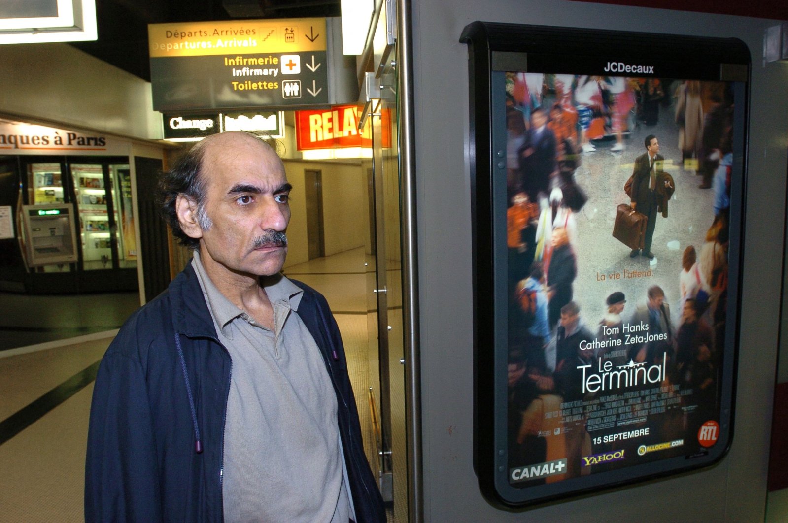 Mehran Karimi Nasseri passes by the poster of the movie inspired by his life, in Terminal 1 of Paris Charles De Gaulle airport, Paris, France, Aug. 12, 2004. (AFP Photo)