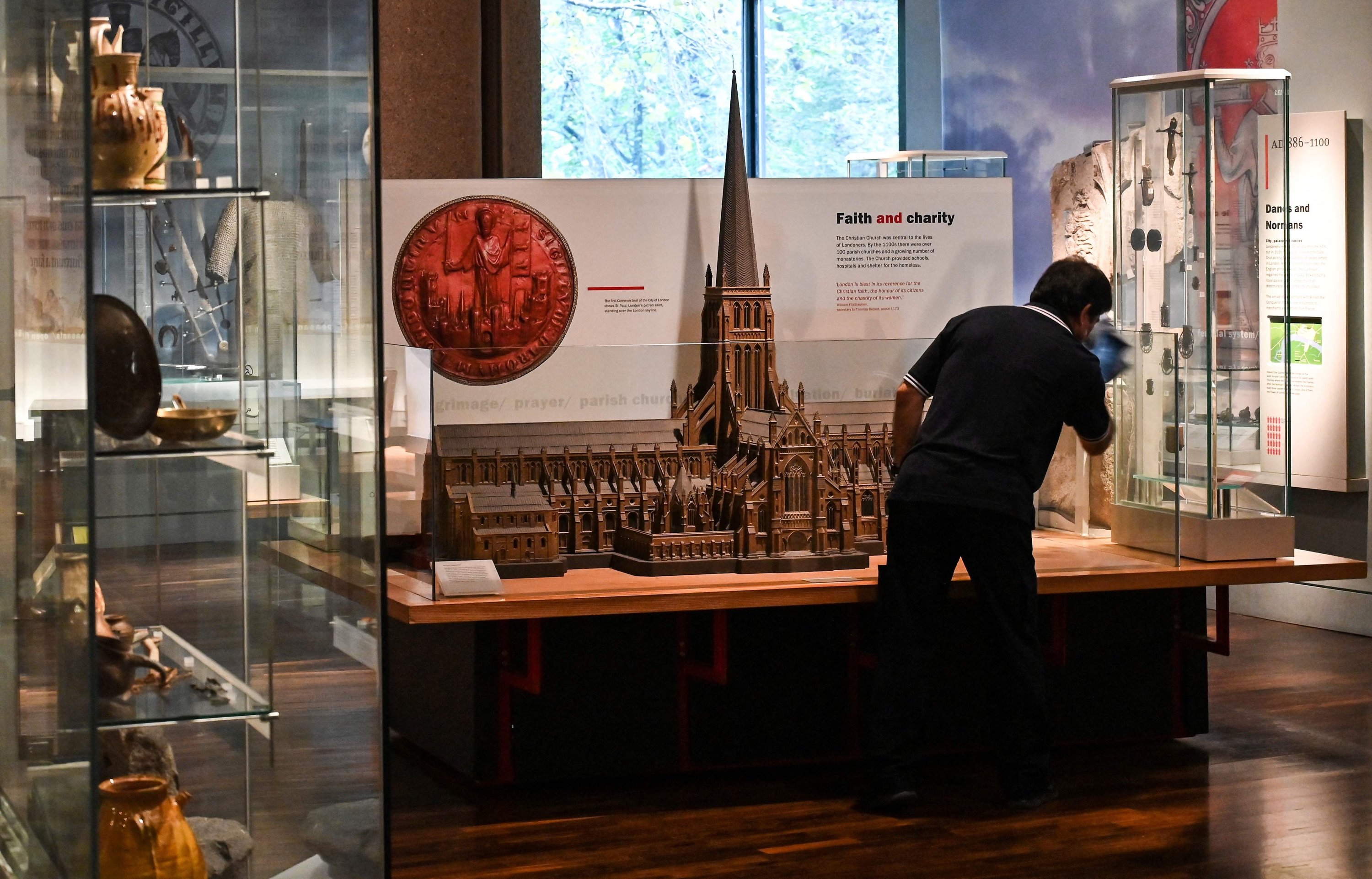 A cleaner wipes down a glass covering the miniature of a gothic church displayed at the Museum of London, London, U.K., Nov. 8 2022. (AFP Photo)