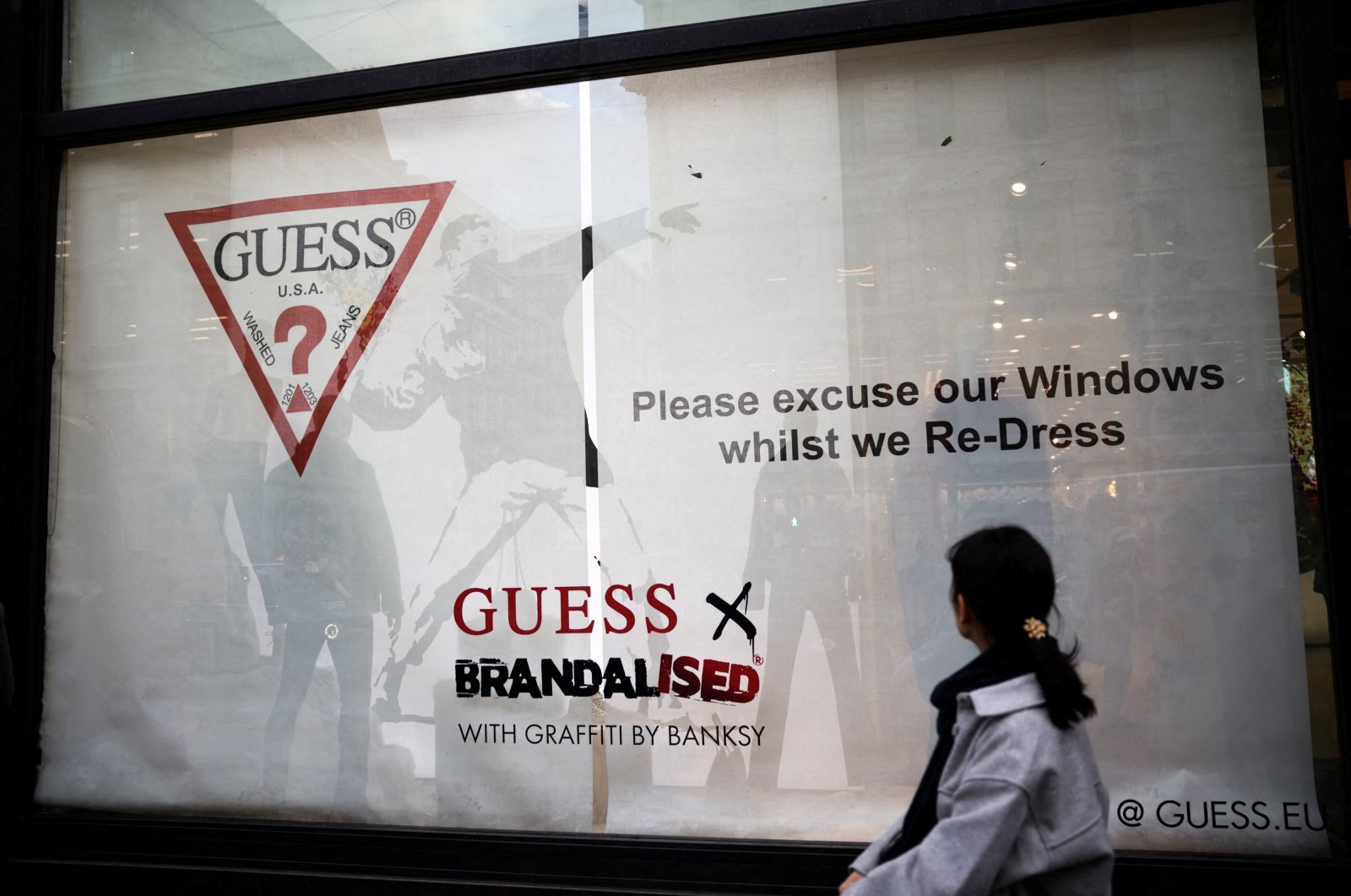 A person walks past the window display of a Guess store that includes the artwork &quot;Flower Thrower&quot; by street artist Banksy, on Regent Street in London, U.K., Nov. 18, 2022. (Reuters Photo)