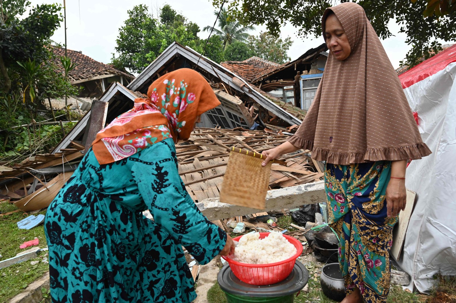 Women cook beside the rubble of a collapsed house in Cugenang, Cianjur, Indonesia, Nov. 23, 2022. (AFP Photo)