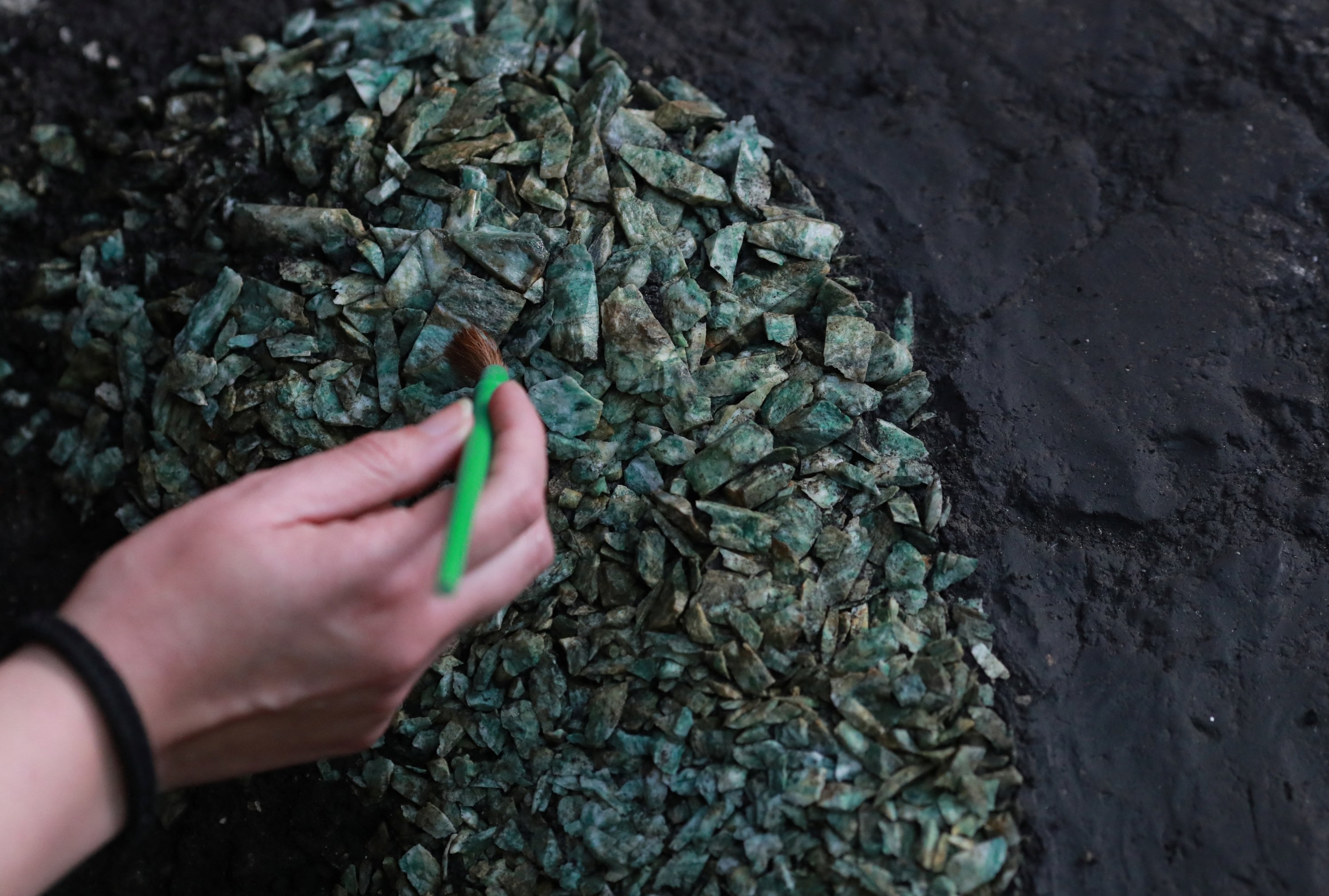 Seorang arkeolog membersihkan persembahan ritual suku Aztec yang menyimpan sejumlah besar fragmen batu hijau berharga, yang pertama dari jenisnya yang pernah ditemukan dan kemungkinan dari bengkel singkat, ditemukan baru-baru ini di sebuah lubang melingkar, Mexico City, Meksiko, 15 November 2022. ( Foto Reuters)