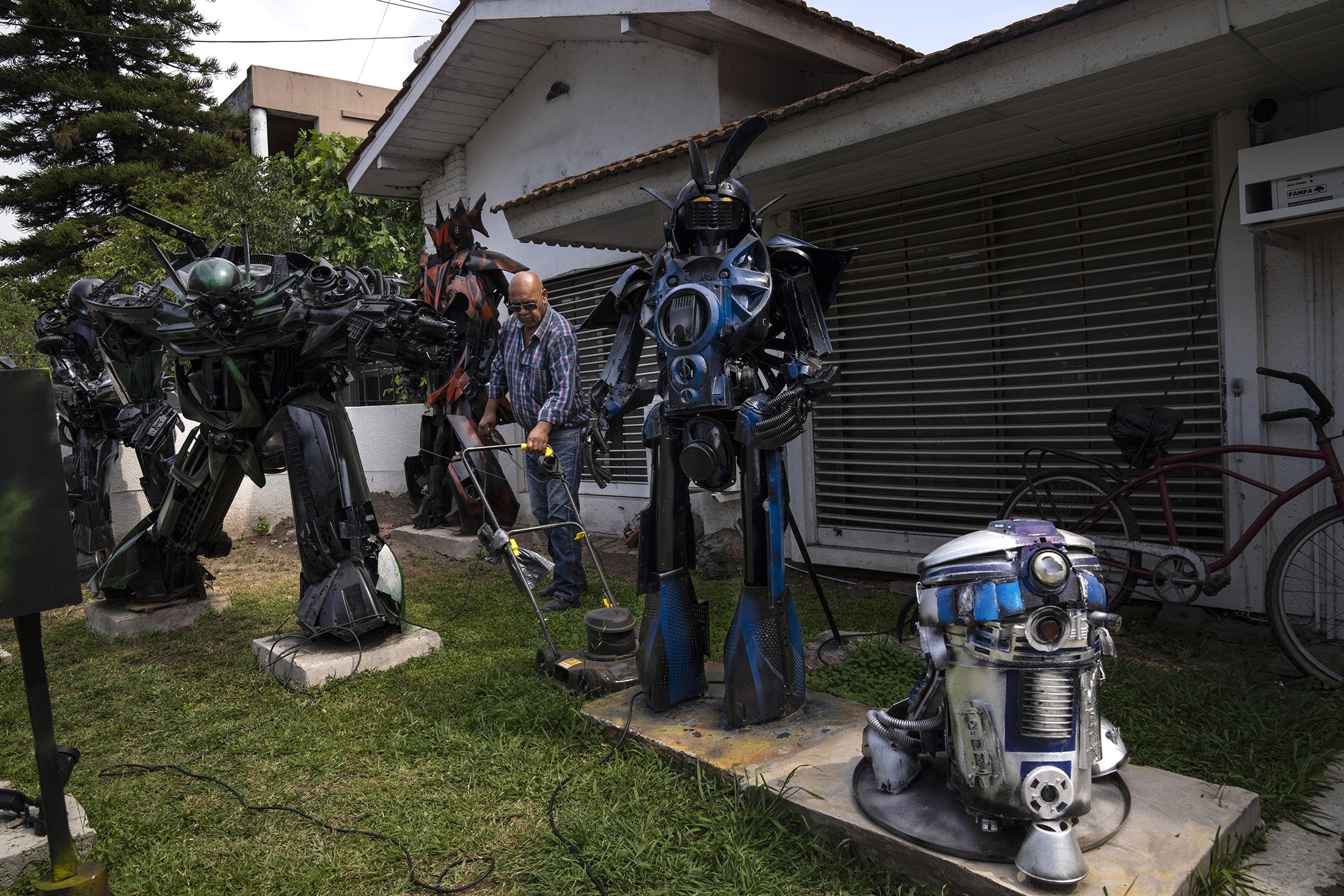 Tukang kebun Juan Acosta memotong halaman depan yang dihiasi beberapa robot menyerupai Transformers, dan replika karakter robot Star Wars R2-D2, di Adrogué, Argentina, 28 Oktober 2022. (Foto AP)