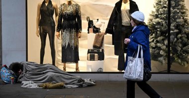 A pedestrian walks past a homeless person sleeping on the floor in front of a clothing shop decorated for Christmas in Chester, U.K., Nov. 17, 2022. (AFP Photo)