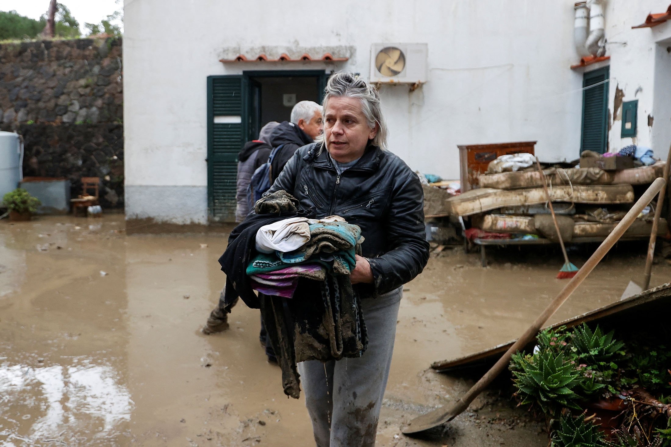 Seorang warga membawa barang-barangnya yang tertutup lumpur setelah tanah longsor di pulau liburan Italia Ischia, Italia, 26 November 2022. (Foto Reuters)
