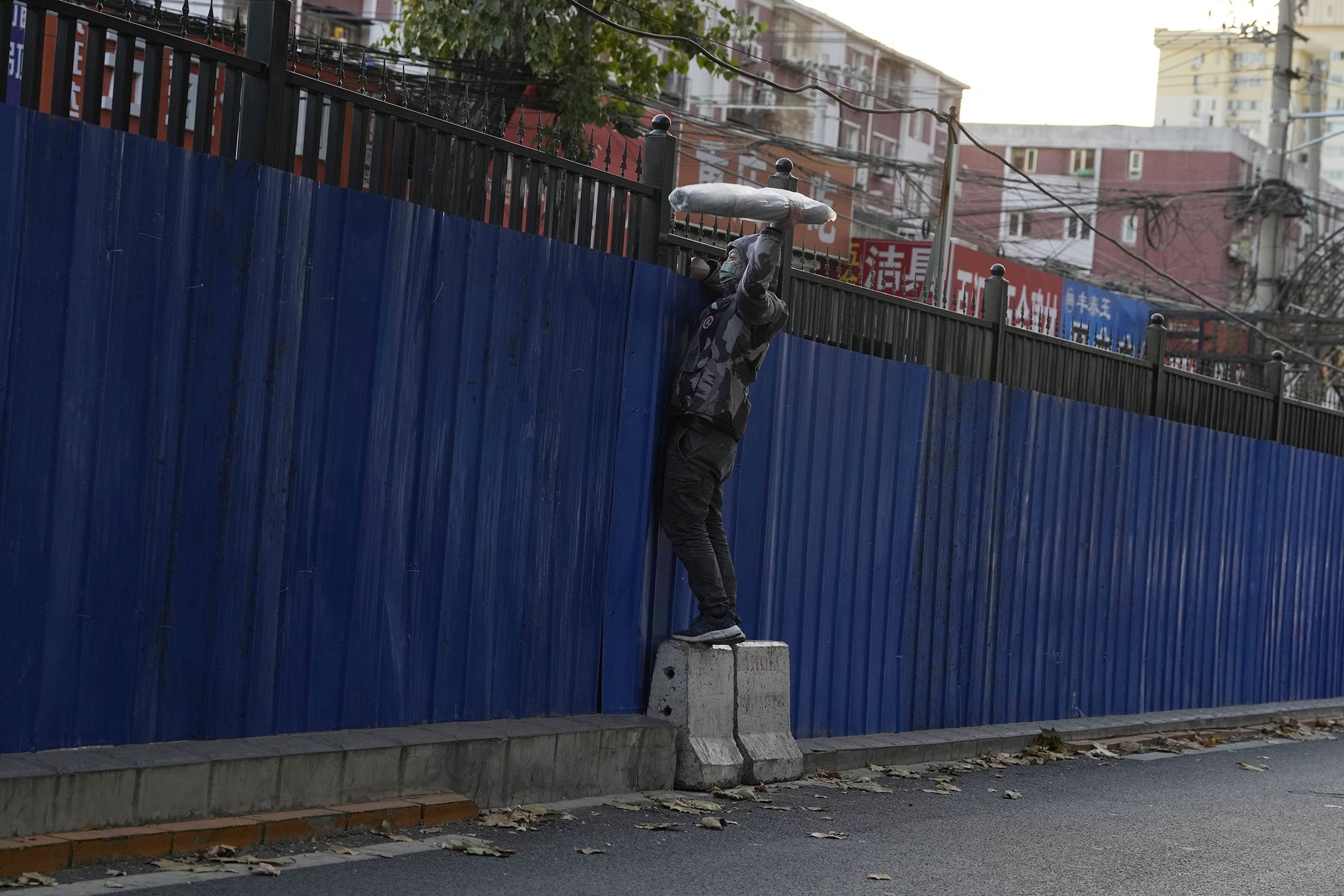 A man retrieves an item through the fences around a community under lockdown in Beijing, China, Nov. 26, 2022. (AP Photo)