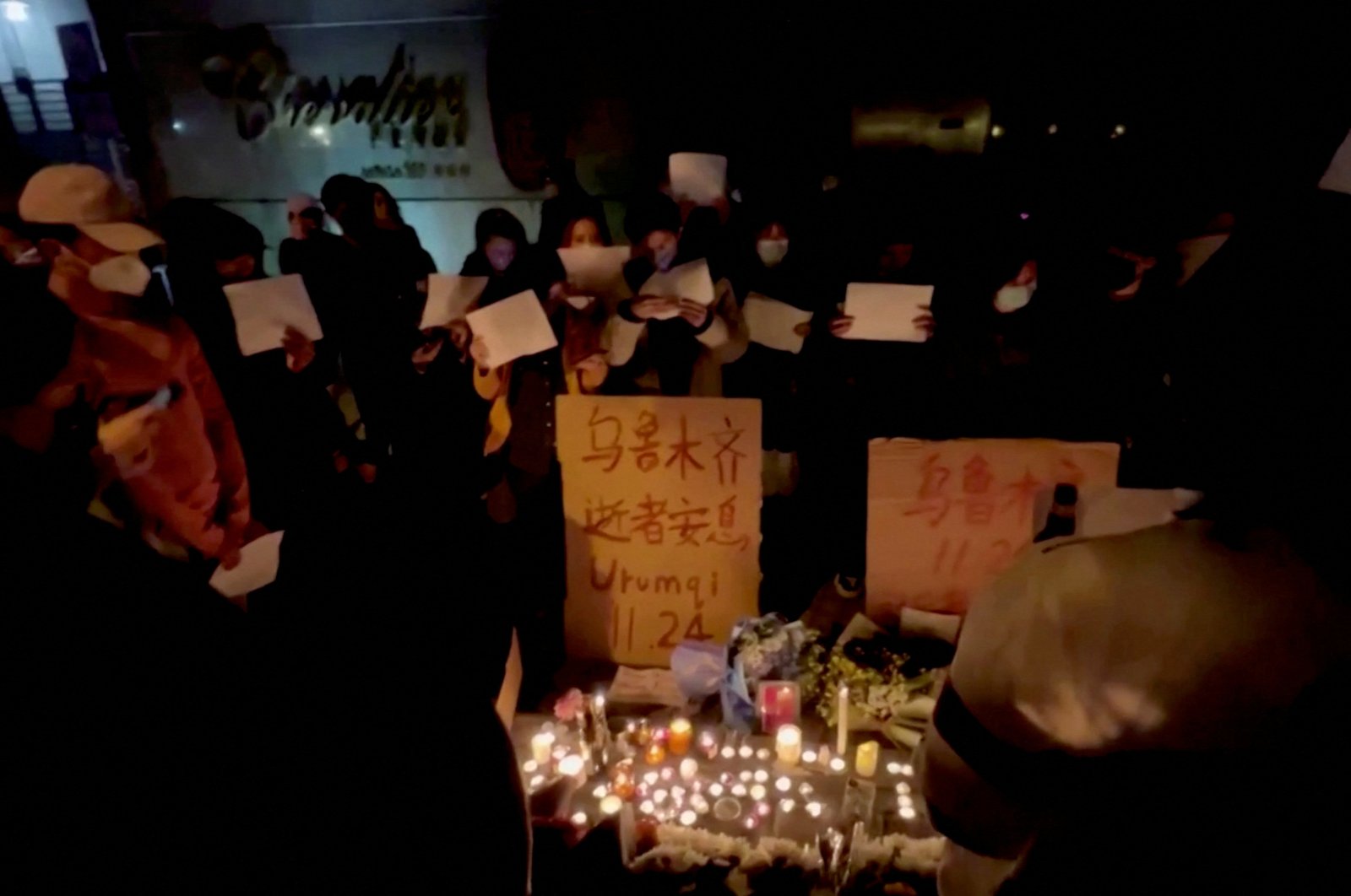 This picture obtained from a social media video shows people holding signs and lighting candles during a vigil held for the victims of the Urumqi fire, in Shanghai, China, Nov. 26, 2022. (Reuters Photo)