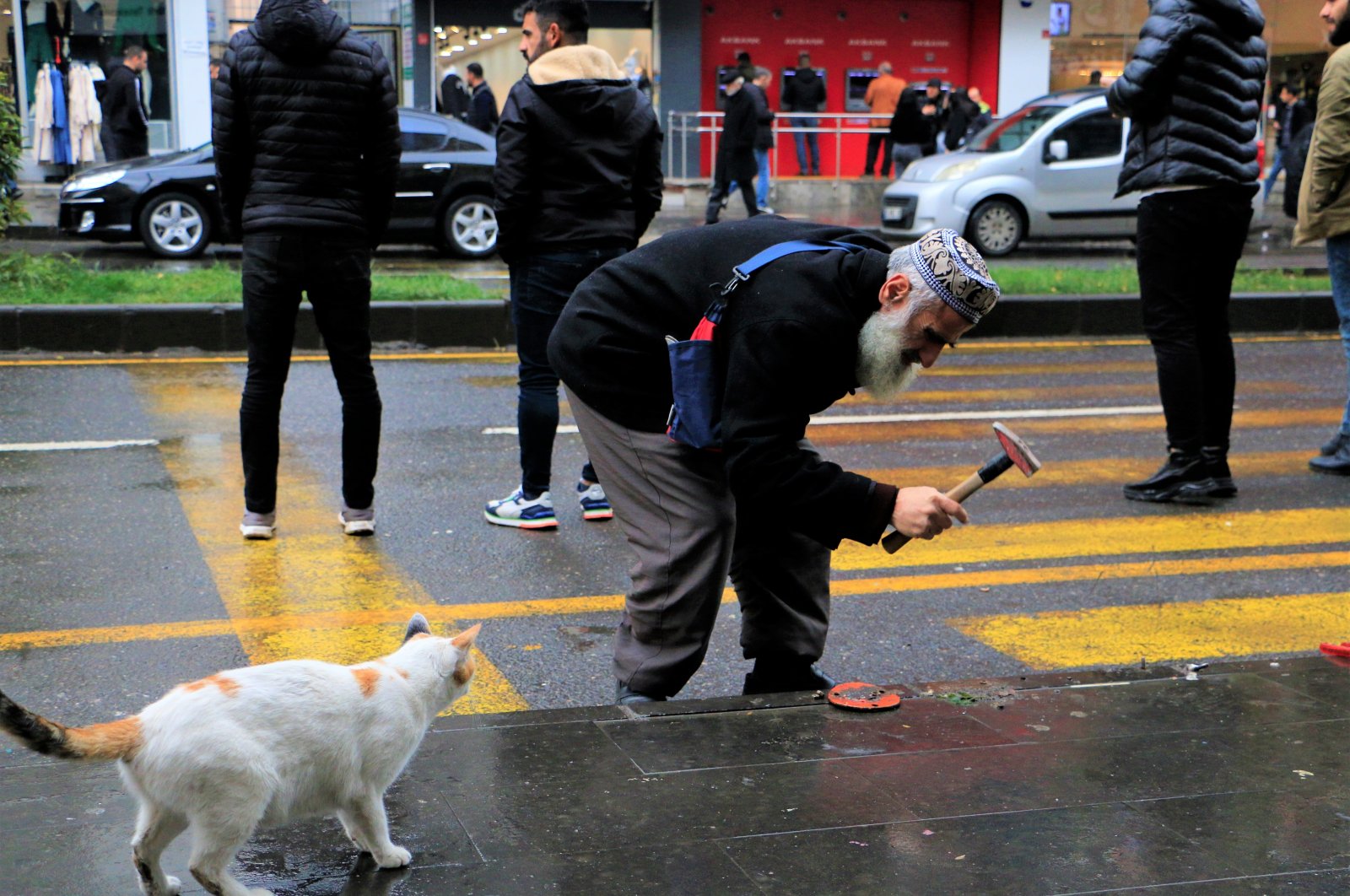 Osama Shafie works to remove a loose screw on a sidewalk, as a cat looks on, in Diyarbakır, southeastern Türkiye, Nov. 29, 2022. (İHA Photo)