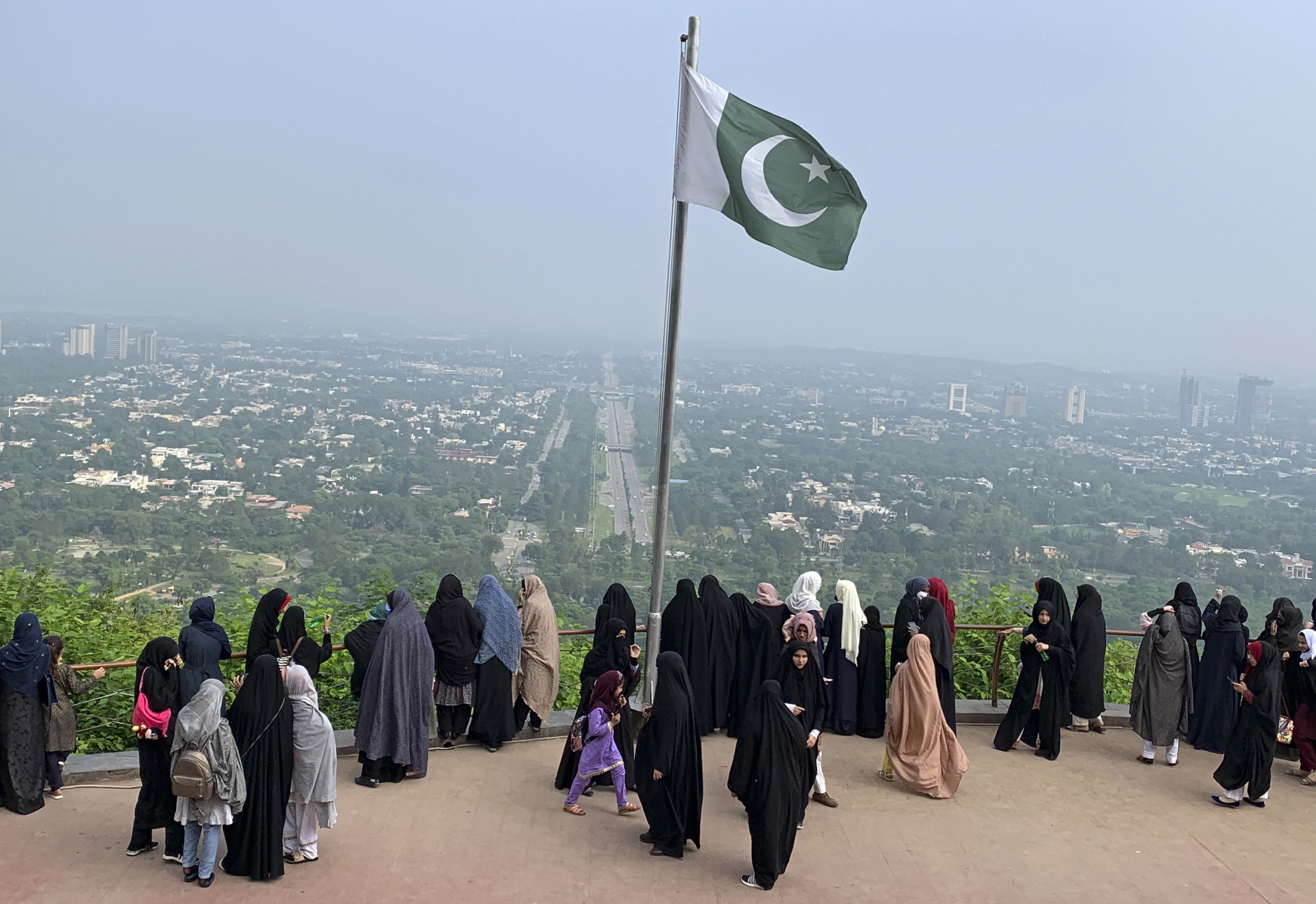 Bendera Pakistan berkibar untuk berjaga-jaga saat para wanita memandang Islamabad, Pakistan, 27 Juli 2022. (Foto AP)