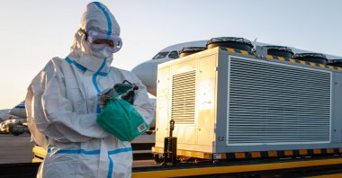 An aircraft ground personnel in a protective suit looks at a phone at the Beijing Capital International Airport, Beijing, China, Nov. 30, 2022. (EPA Photo)
