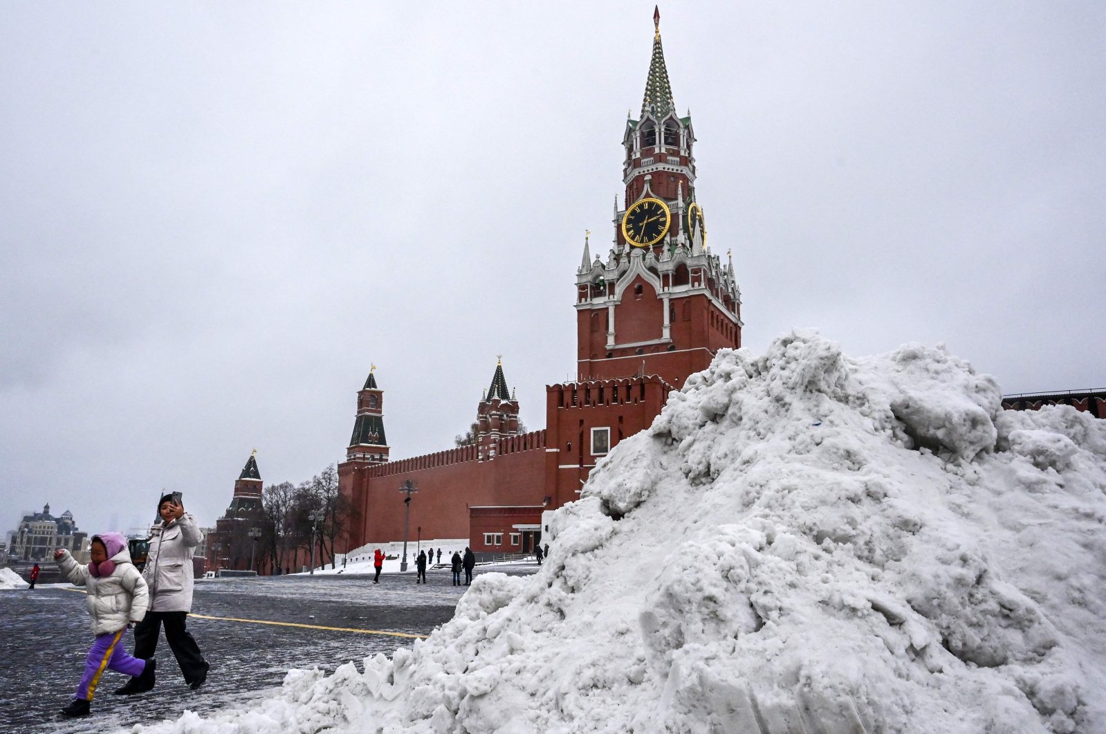 Children walk past a snow heap after a snowfall in front of the Spasskaya tower of the Kremlin, Moscow, Russia, Nov. 22, 2022. (AFP Photo)