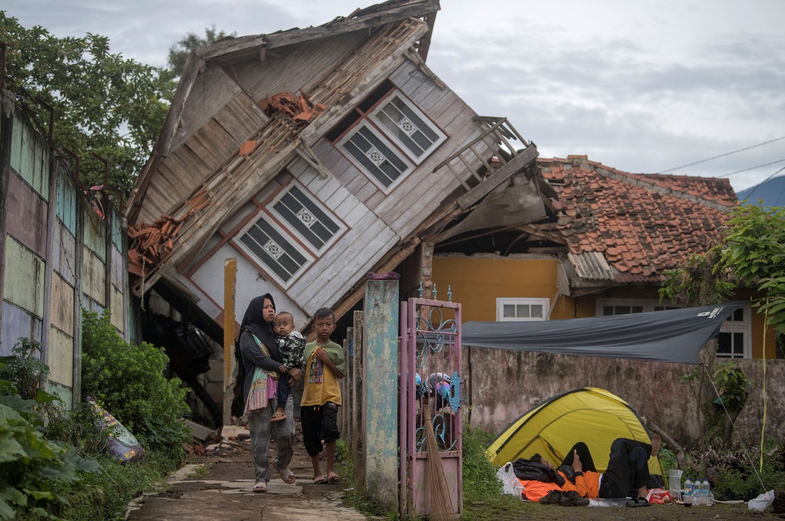A woman carrying her child walks near a badly damaged house after earthquake in Cianjur, West Java province, Indonesia, Nov. 25, 2022. (Reuters Photo)