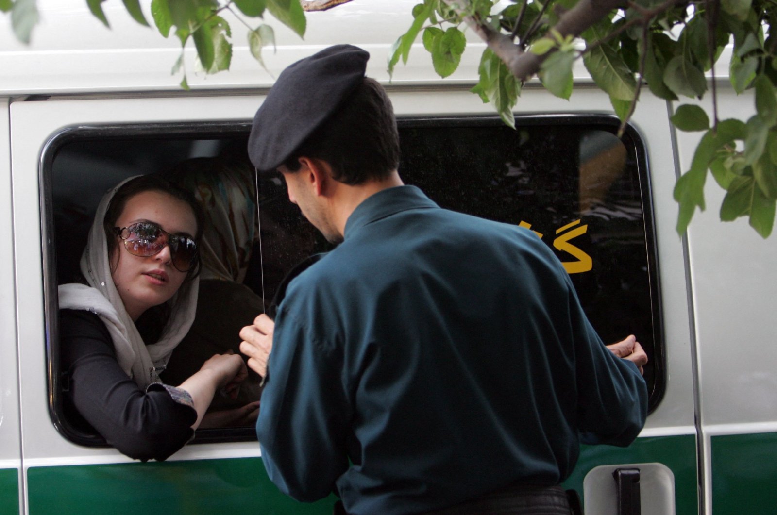An Iranian policeman speaks with a woman sitting in a police car after she was arrested because of her &quot;inappropriate&quot; clothes, Tehran, Iran, July 23, 2007. (AFP Photo)