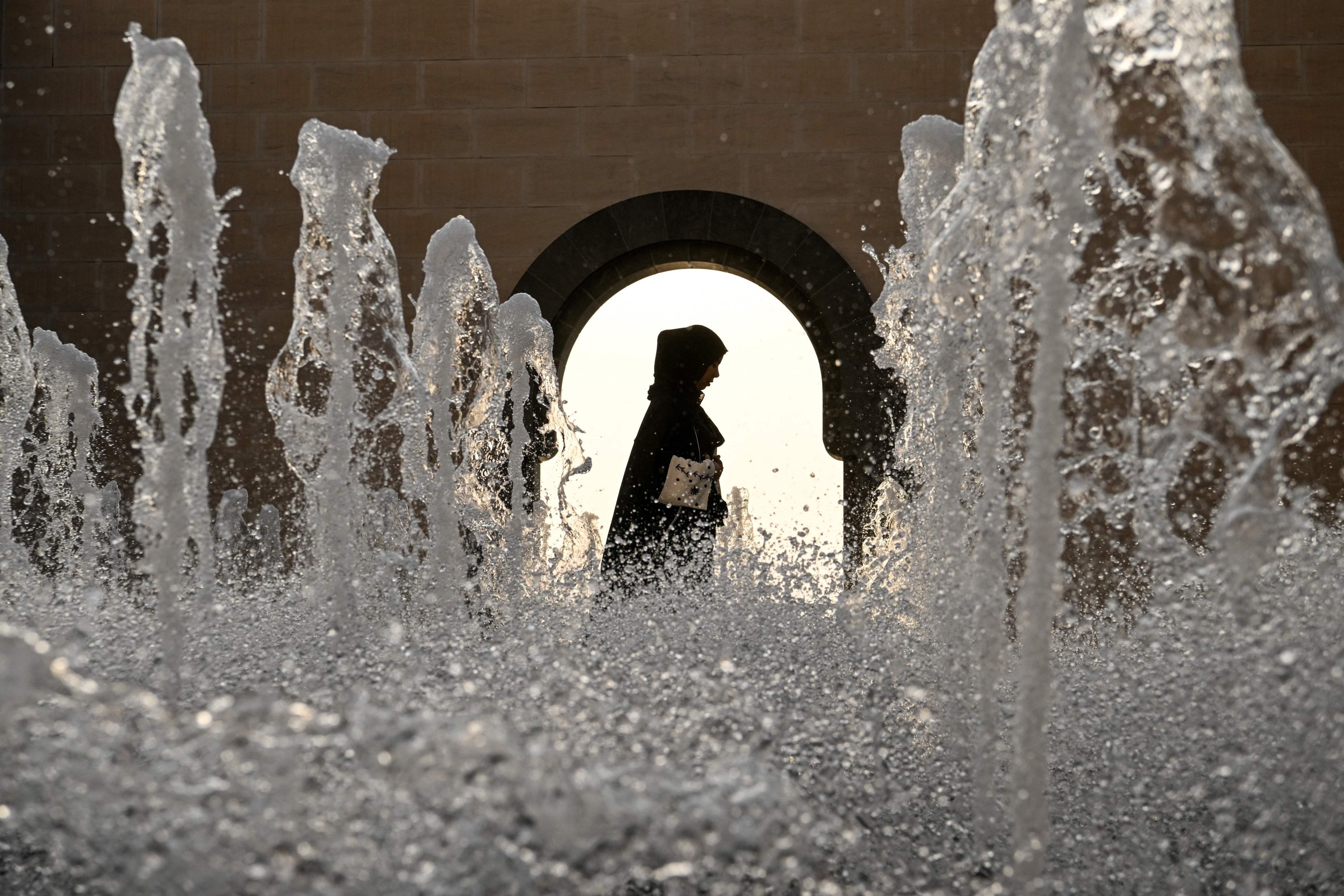 Seorang wanita berjalan melewati air mancur di balkon Museum Seni Islam di Doha, jelang turnamen sepak bola Piala Dunia Qatar 2022, Qatar, 13 November 2022. (AFP Photo)