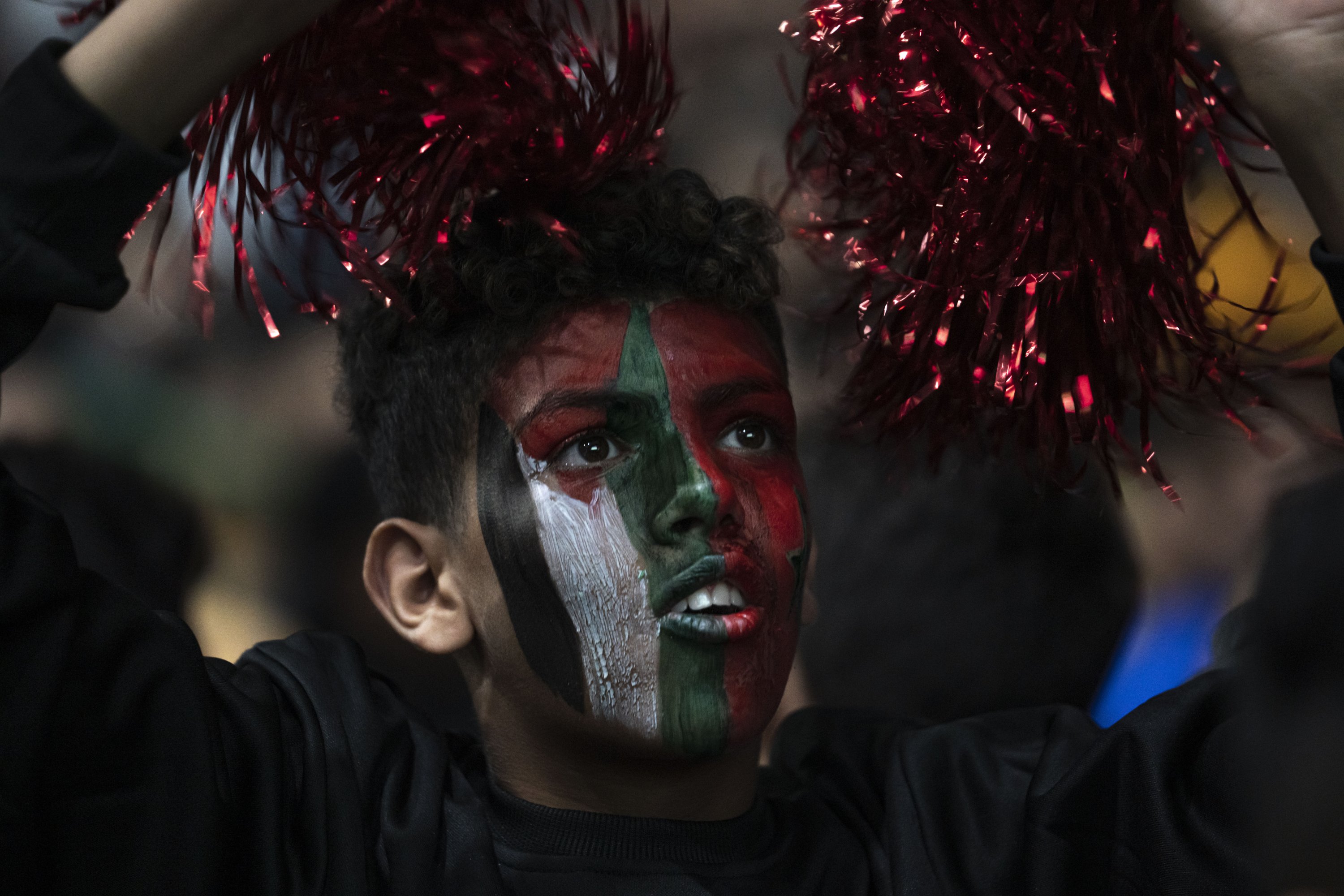 Seorang penggemar Maroko dengan wajah dicat dengan bendera Maroko dan Palestina menyaksikan siaran langsung pertandingan sepak bola perempat final Piala Dunia antara Maroko dan Portugal yang dimainkan di Qatar, di Kota Gaza, Palestina, 10 Desember 2022. (Foto AP)