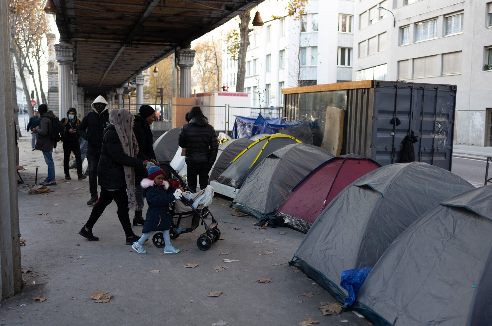 People walk near migrant tents as the Mayor of Paris with members of associations in solidarity with migrants visits a refugee camp (migrant camp) under the aerial metro on the Boulevard de la Chapelle in Paris on Dec. 9, 2022. (Reuters File Photo)