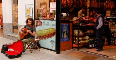 A street musician plays a guitar as a worker cuts ham in a shop in Ronda, southern Spain, April 27, 2022. (Reuters Photo)