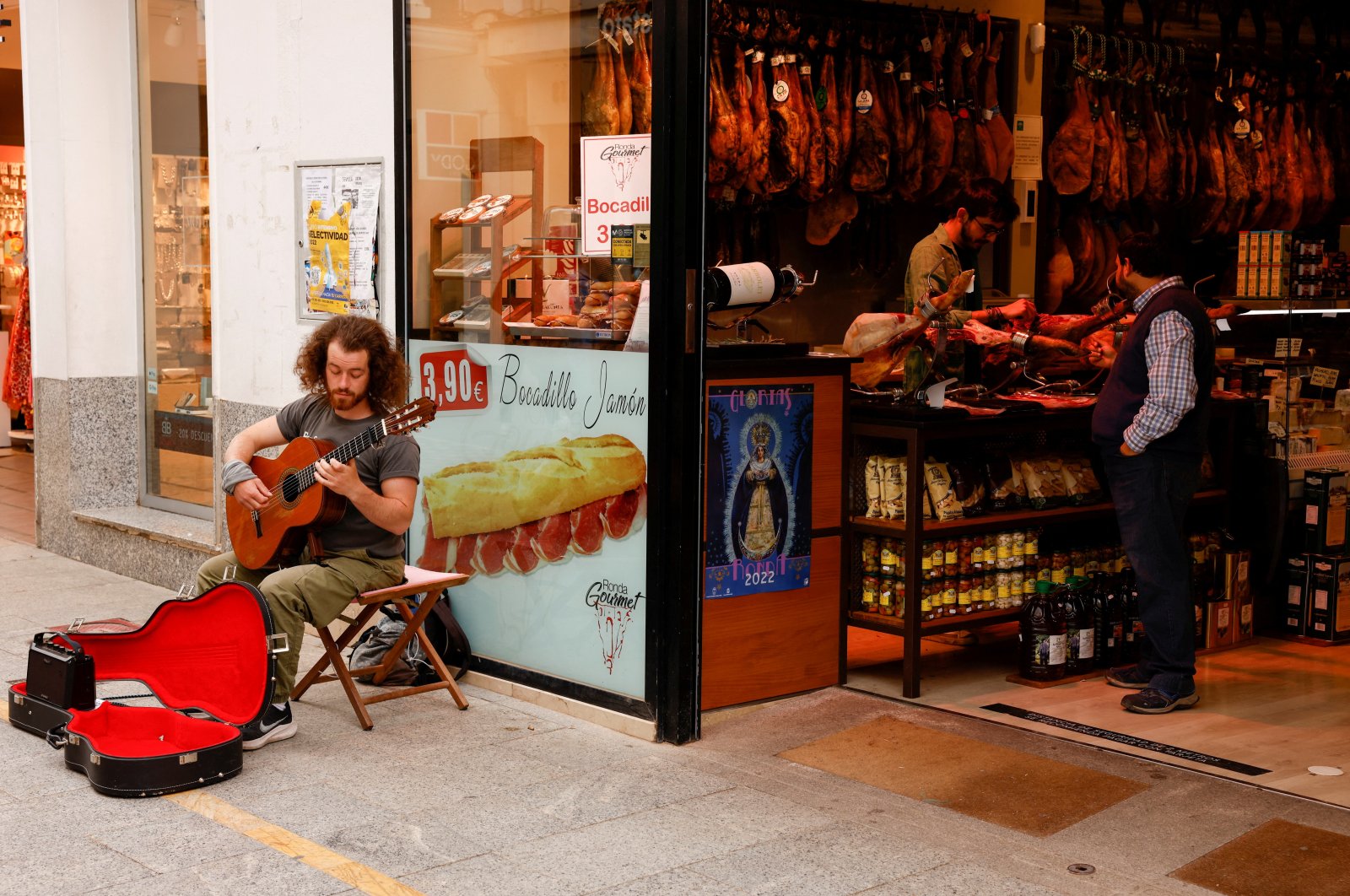 A street musician plays a guitar as a worker cuts ham in a shop in Ronda, southern Spain, April 27, 2022. (Reuters Photo)