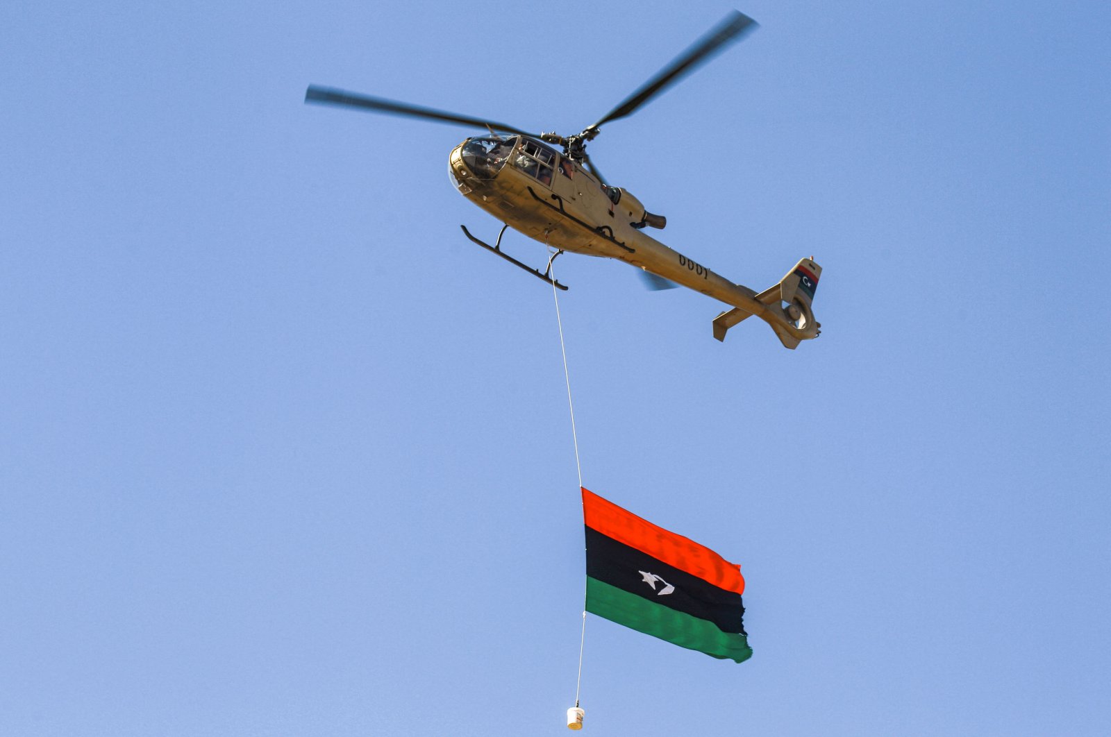 A military helicopter flies with the Libyan national flag hanging underneath at a rally marking the 71st anniversary of the country&#039;s independence from Italy in the eastern city of Benghazi on Dec. 24, 2022. (AFP Photo)