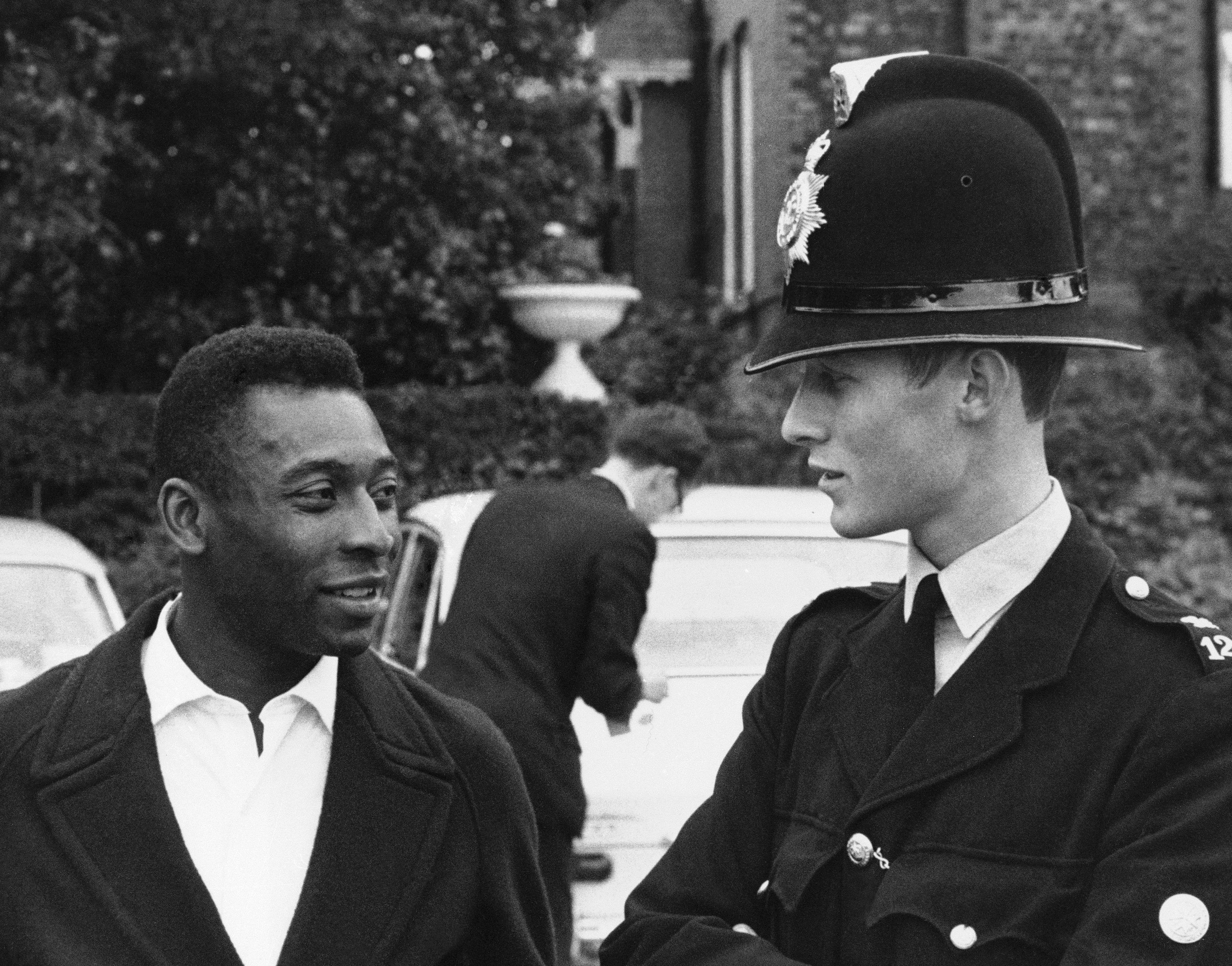 Pemain sepak bola terkenal Pele berbicara untuk mengadakan percakapan dengan seorang polisi setelah tim Brasil tiba di hotel mereka, Chester, Inggris, Juli 1966. (Foto AP)