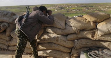 A YPG terrorist looks through binoculars toward Syrian National Army (SNA) positions, at the front line in the village of Halawanji, north of Manbij, Syria, March 29, 2018. (AP Photo)