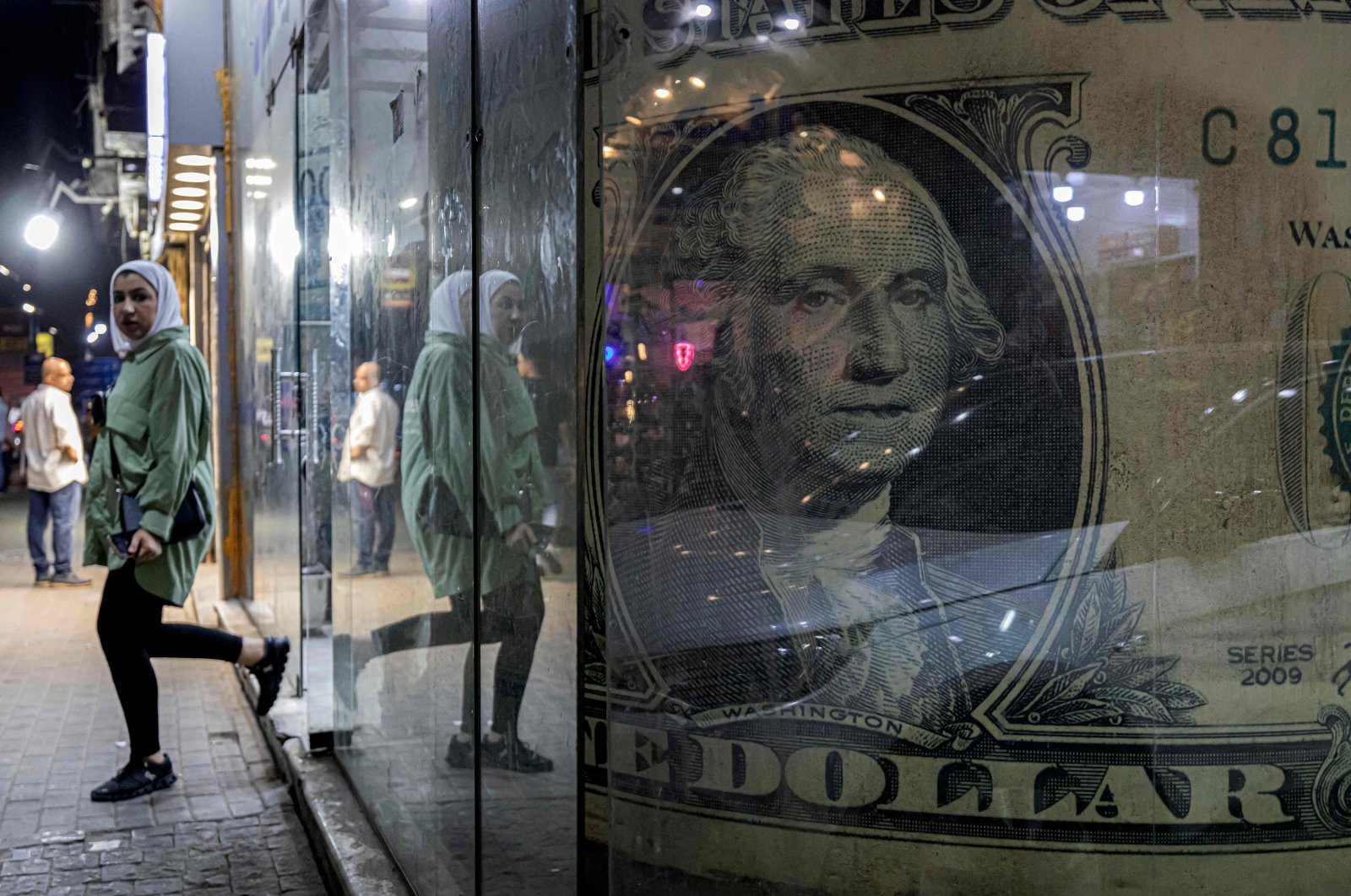 A woman walks out of a currency exchange shop displaying a giant U.S. dollar banknote in the Zamalek district of Cairo, Egypt, Aug. 24, 2022. (AFP Photo)