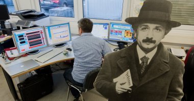 An employee sits in front of screens in the gravitational waves detector next to a cardboard display of Albert Einstein, Lower Saxony, Sarstedt, Germany, Jan. 22, 2019. (Getty Images)