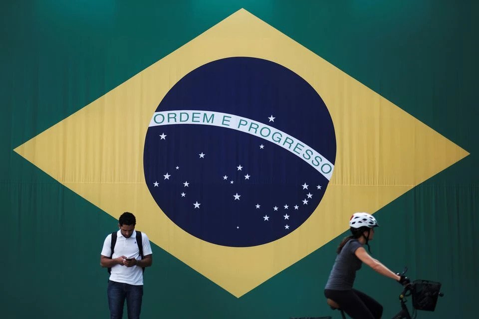 A man checks his mobile phone as a woman riding a bike passes next to a big Brazilian flag in Sao Paulo, Brazil, June 28, 2018. (Reuters File Photo)