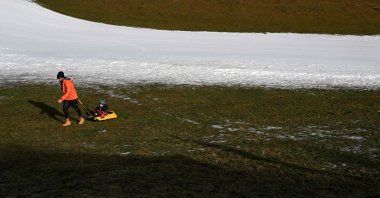 A man pulls a child on a sled next to an artificial snow slope in Filzmoos, Austria, Jan. 6, 2023. (AFP Photo)