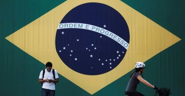 A man checks his mobile phone as a woman riding a bike passes next to a big Brazilian flag in Sao Paulo, Brazil, June 28, 2018. (Reuters File Photo)