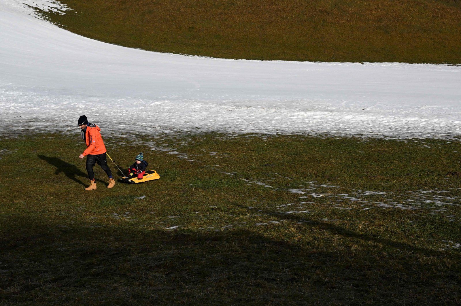 A man pulls a child on a sled next to an artificial snow slope in Filzmoos, Austria, Jan. 6, 2023. (AFP Photo)