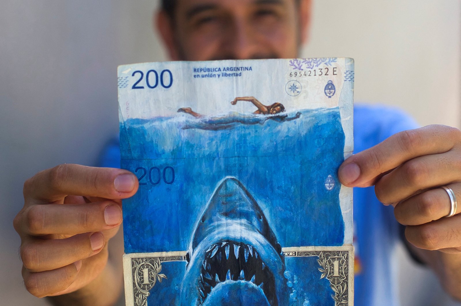 Artist Sergio Diaz holds intervened Argentine pesos bills and a U.S. dollar bill depicting Steven Spielberg&#039;s movie &quot;Shark&quot; as a parody of Argentina&#039;s ever-increasing inflation, in Salta, Argentina, Dec. 30, 2022. (Reuters Photo)