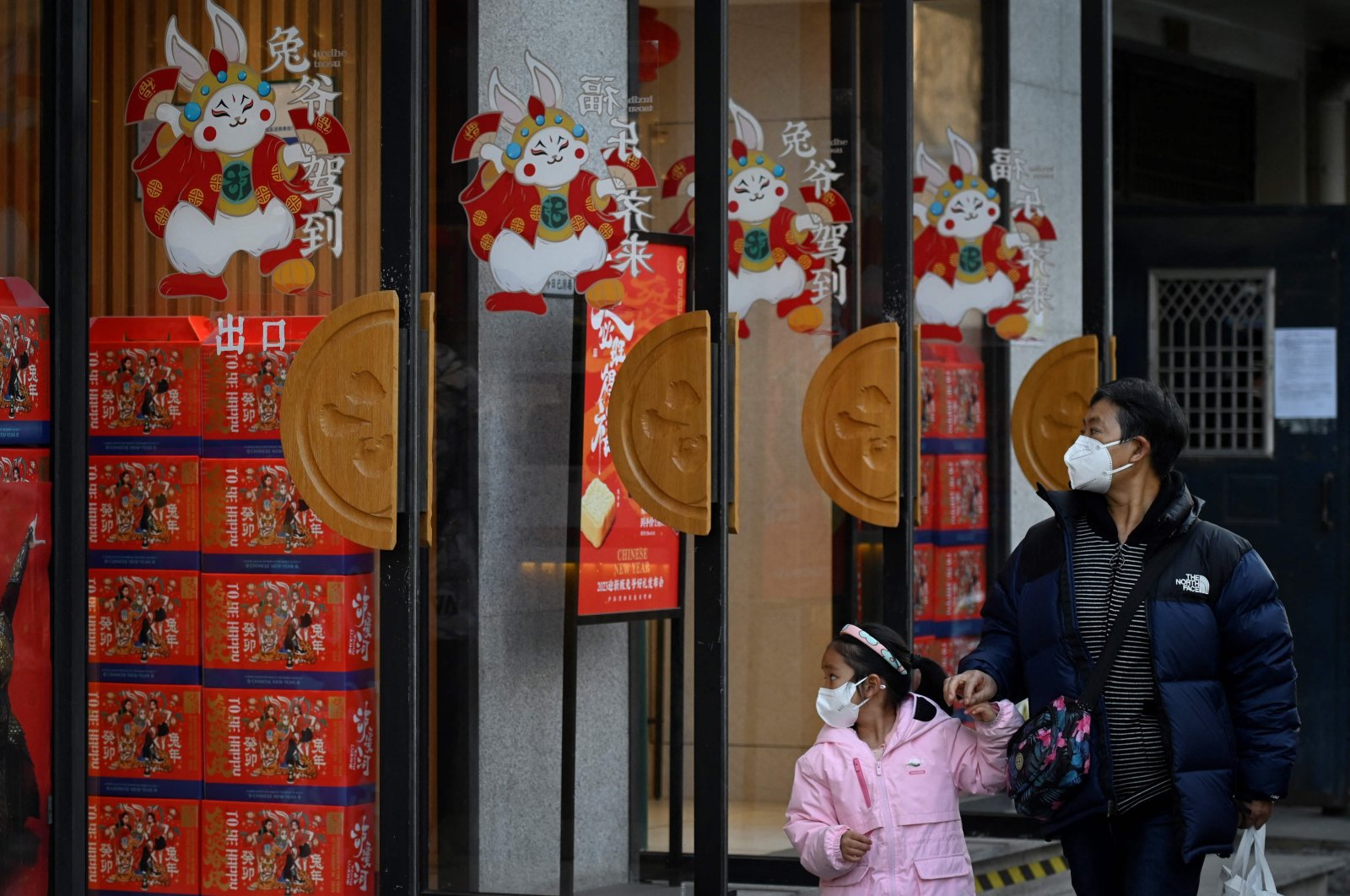 A man and a child walk past a bread shop decorated with rabbit patterns on doors, Beijing, Jan. 10, 2023. (AFP Photo)