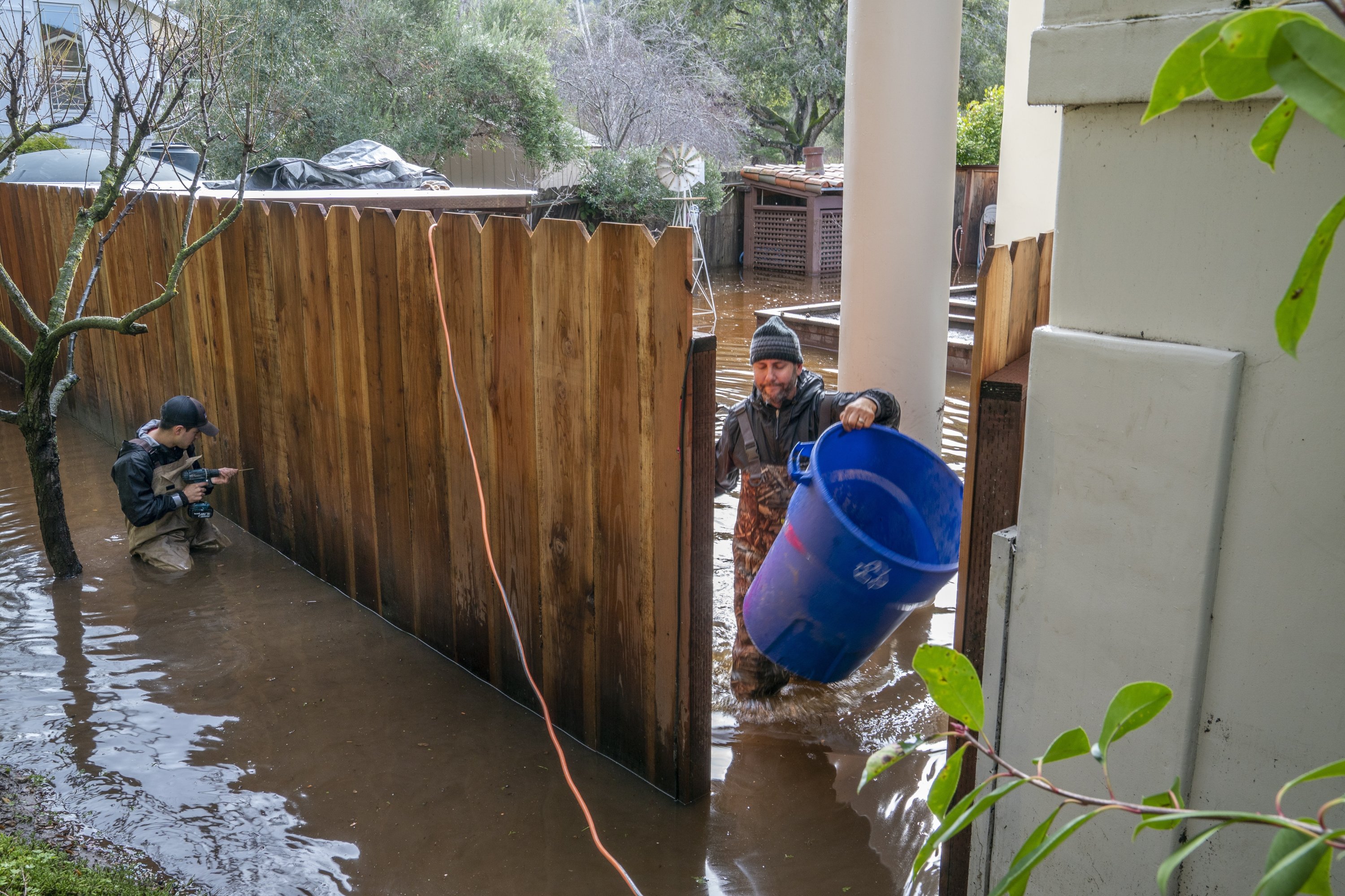Penduduk setempat membersihkan air banjir dari halaman belakang mereka setelah gelombang badai lainnya di Carmel, California, AS, 10 Januari 2023. (Foto EPA)