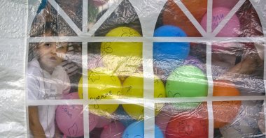 A boy stands next to balloons carrying the names of deceased children during an event to commemorate children that died at a very early age due to health problems, Bucharest, Romania, May 26, 2013. (AP Photo)
