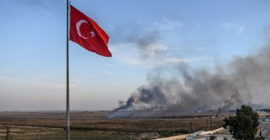 Smoke rises from the Syrian town of Tal Abyad, in a picture taken from the Turkish side of the border where the Turkish flag is seen near Akçakale on Oct. 10, 2019. (AFP File Photo)