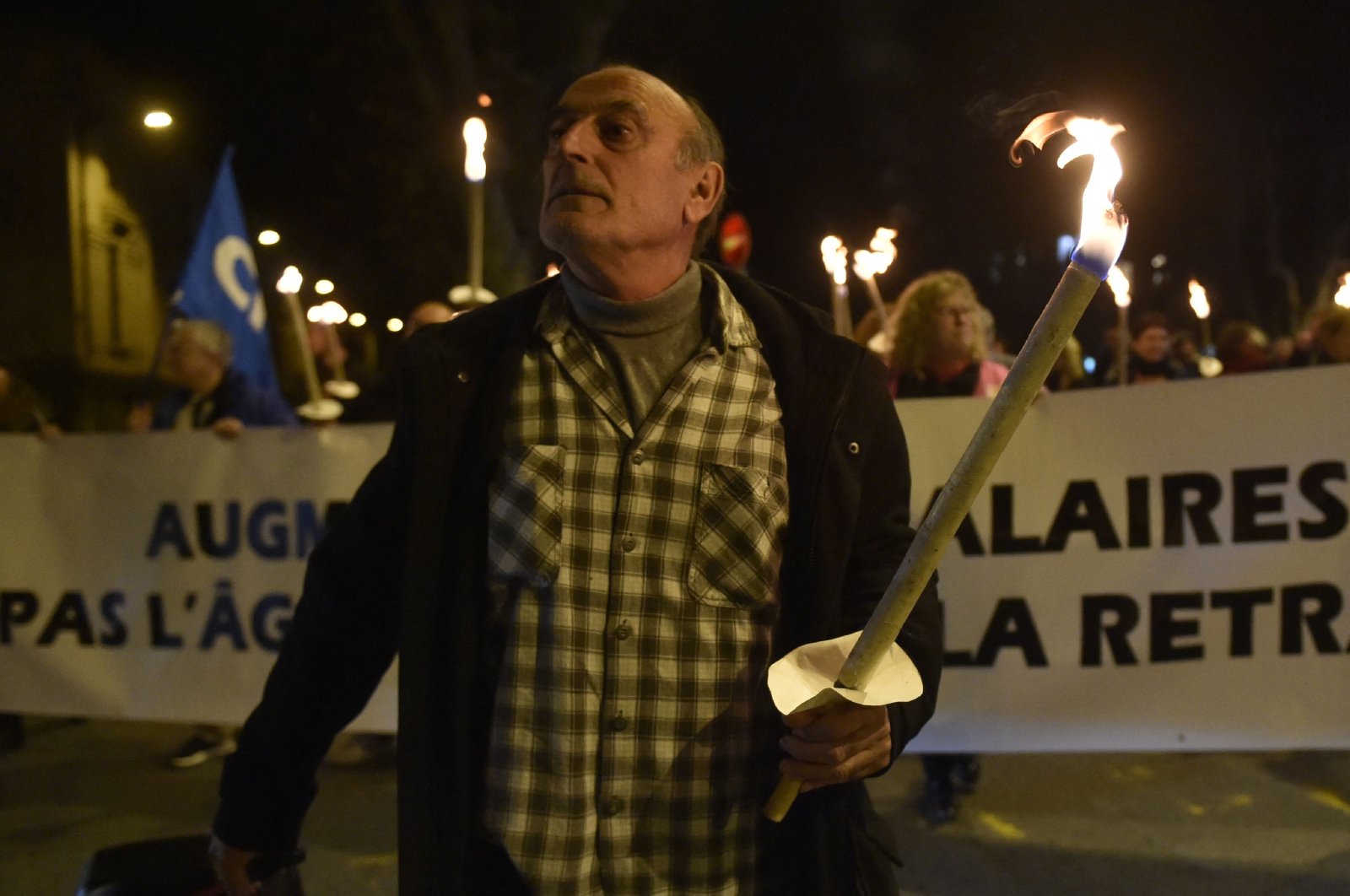 A man leads demonstrators holding torches and a banner that reads "let&#039;s raise salaries not the retirement age," in Perpignan, southern France, Jan. 10, 2023. (AFP Photo)