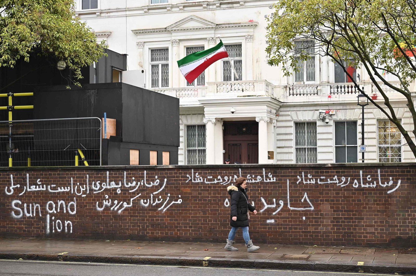 Pedestrians walk past graffiti daubed on a wall outside the Iranian Embassy in London on Jan. 14, 2023. (AFP Photo)