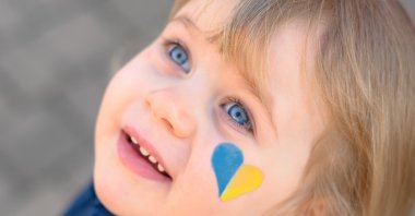 Portrait of a little Ukrainian girl with a hopeful look and a bicolour blue yellow heart on the cheek. (Shutterstock Photo)
