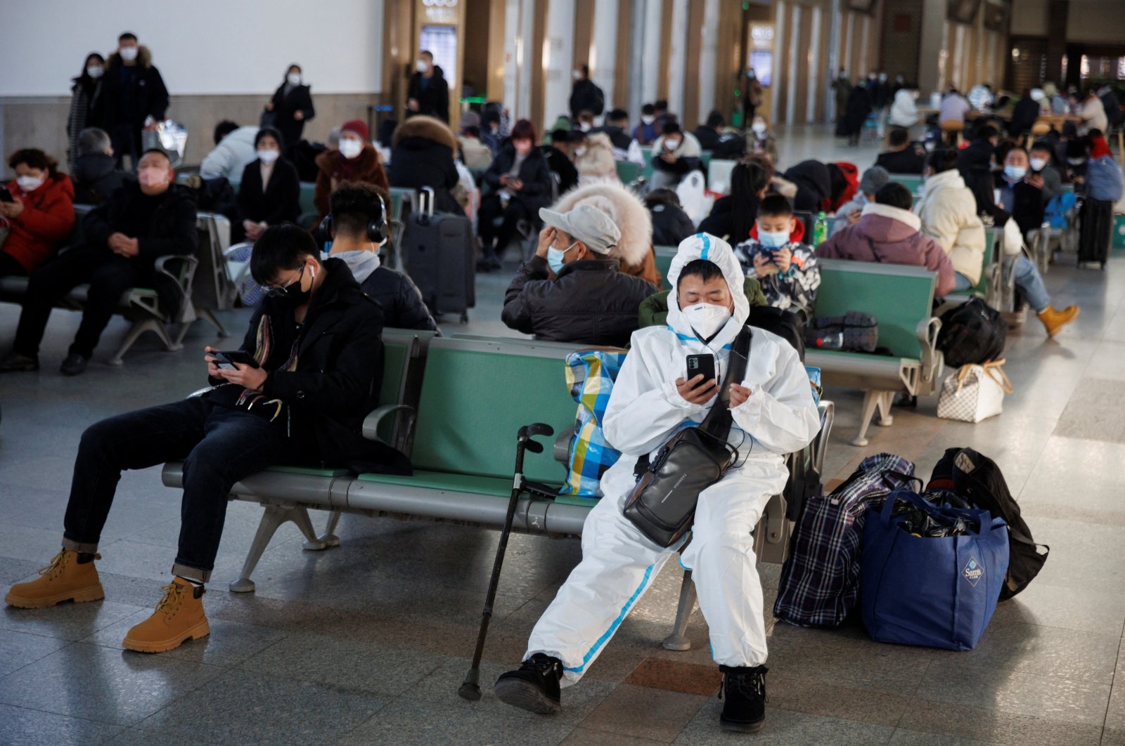 A person wearing a protective suit sits in Beijing Railway Station as passengers wait to board a train to travel for Spring Festival ahead of Chinese Lunar New Year festivities after China lifted its COVID-19 restrictions, Beijing, China, Jan. 20, 2023. (Reuters Photo)